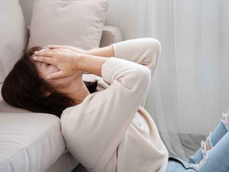 Persona sentada en el suelo cubriéndose el rostro con las manos, reflejando ansiedad y miedo relacionado con la salud y el diagnóstico de VIH.