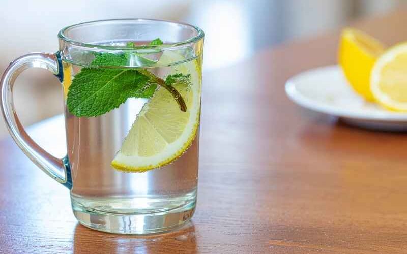 Vaso con agua, limón y hojas de menta sobre una mesa, asociado a la hidratación como hábito para cuidar las vías urinarias.
