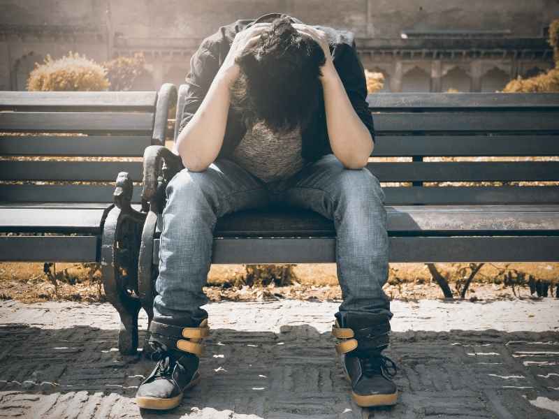 Persona sentada en una banca con la cabeza entre las manos, representando estrés, miedo y estigma alrededor del VIH.
